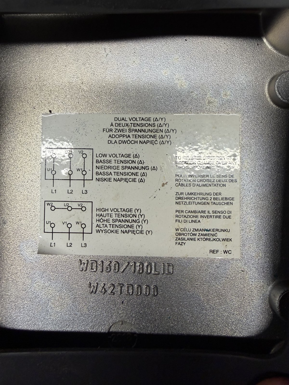 Brook Crompton connection label inside a motor terminal box lid showing dual voltage delta/star diagrams with W2 U2 V2 over U1 V1 W1, low voltage delta with vertical links, high voltage star with the top row bridged, and the instruction to reverse rotation by changing over any two supply lines