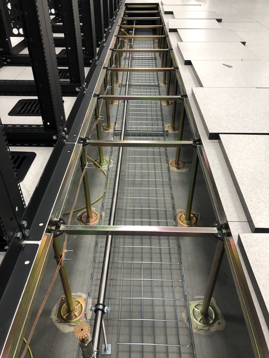 BMS vs DCIM — basket tray under a data centre raised floor beside a row of rack frames