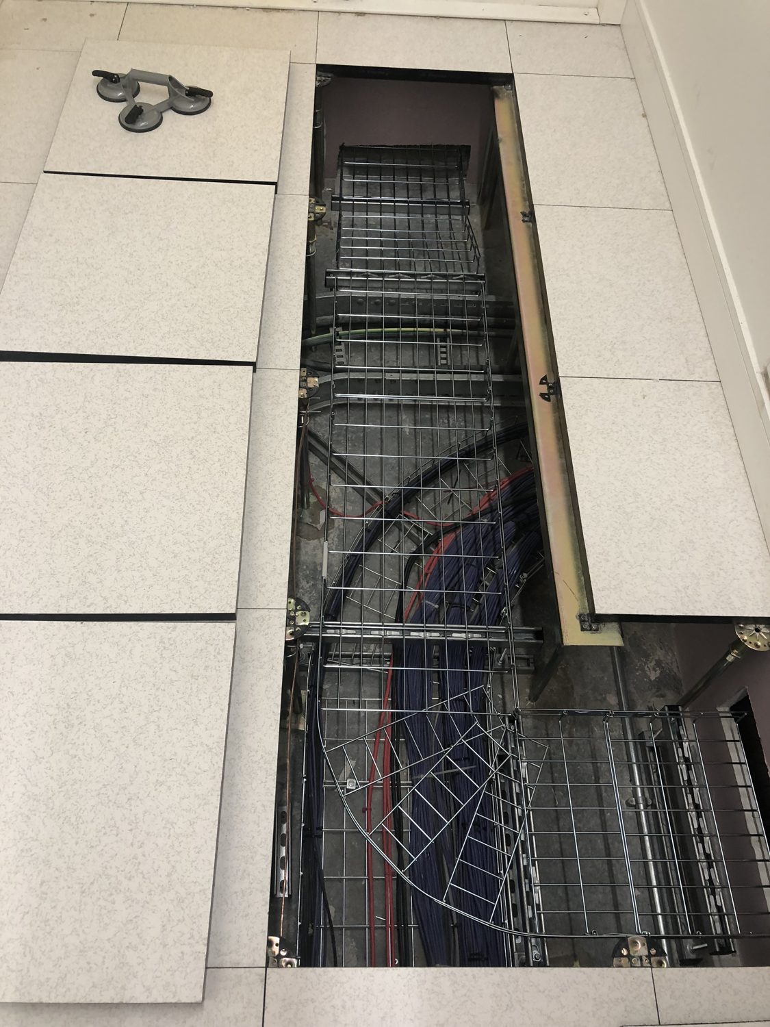 Data centre BMS integration — raised floor tiles lifted to show basket tray and cabling in the underfloor void