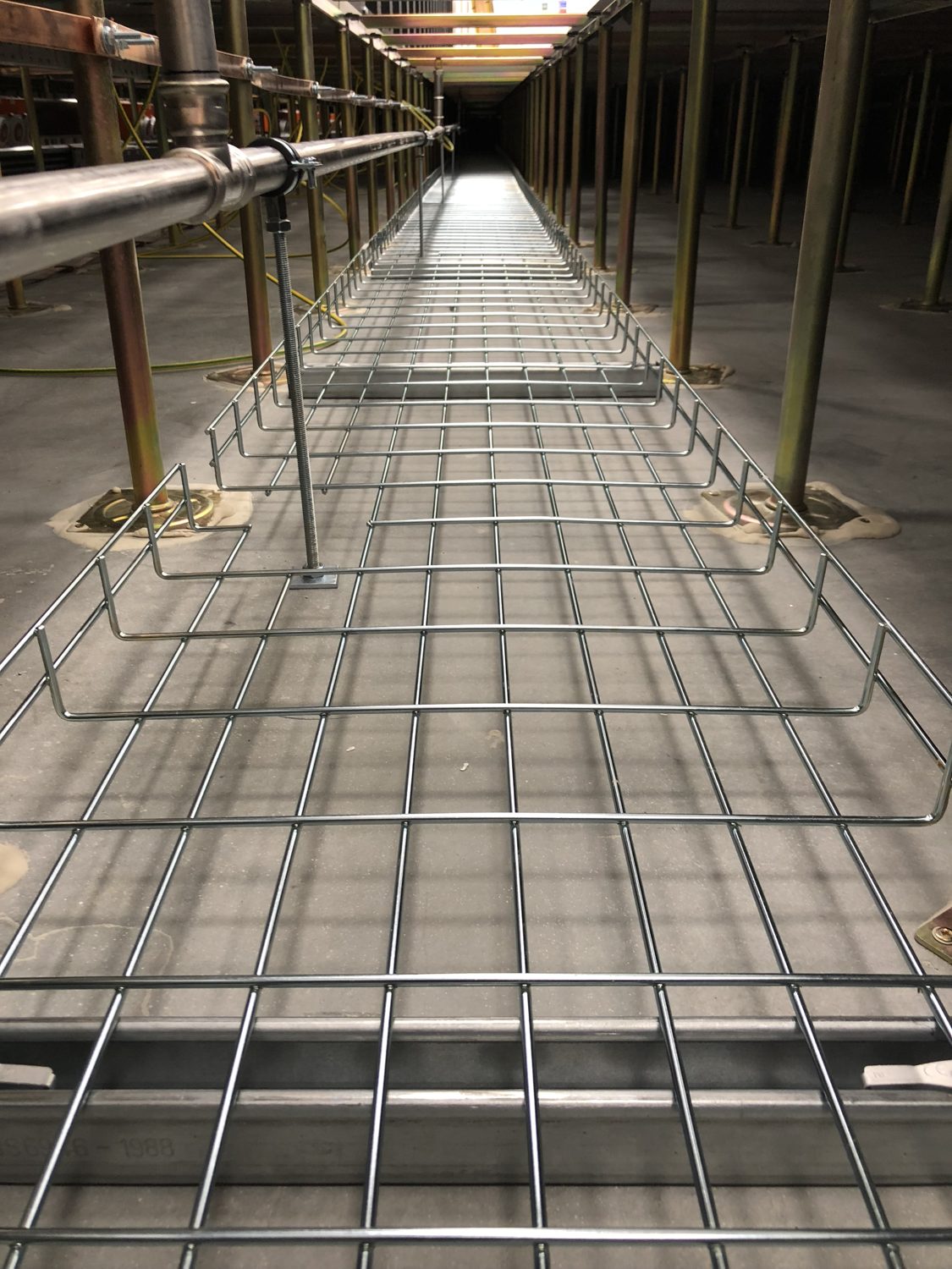 Data centre BMS alarm management — basket tray running through the underfloor void of a data centre raised floor