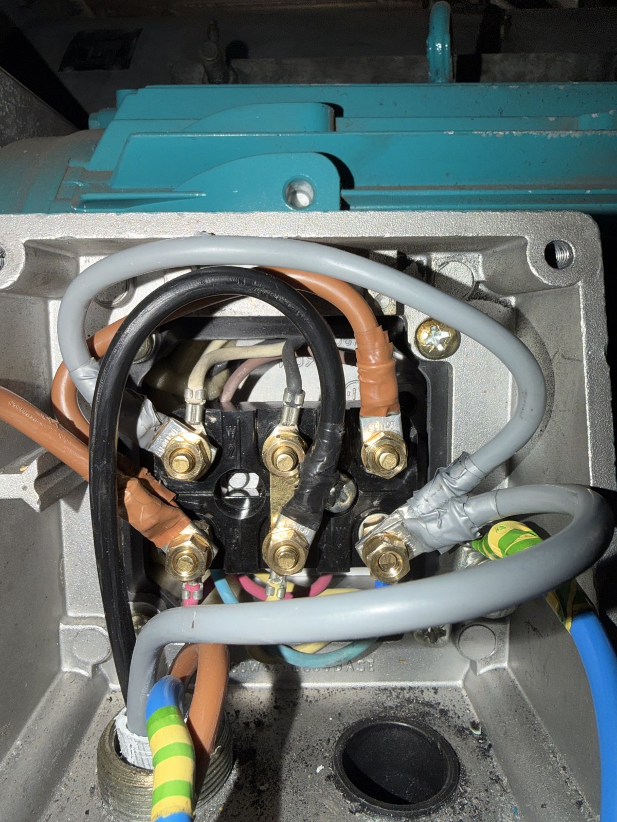 Open three-phase motor terminal box showing six brass studs in two rows with vertical delta link strips and the supply cores being reconnected