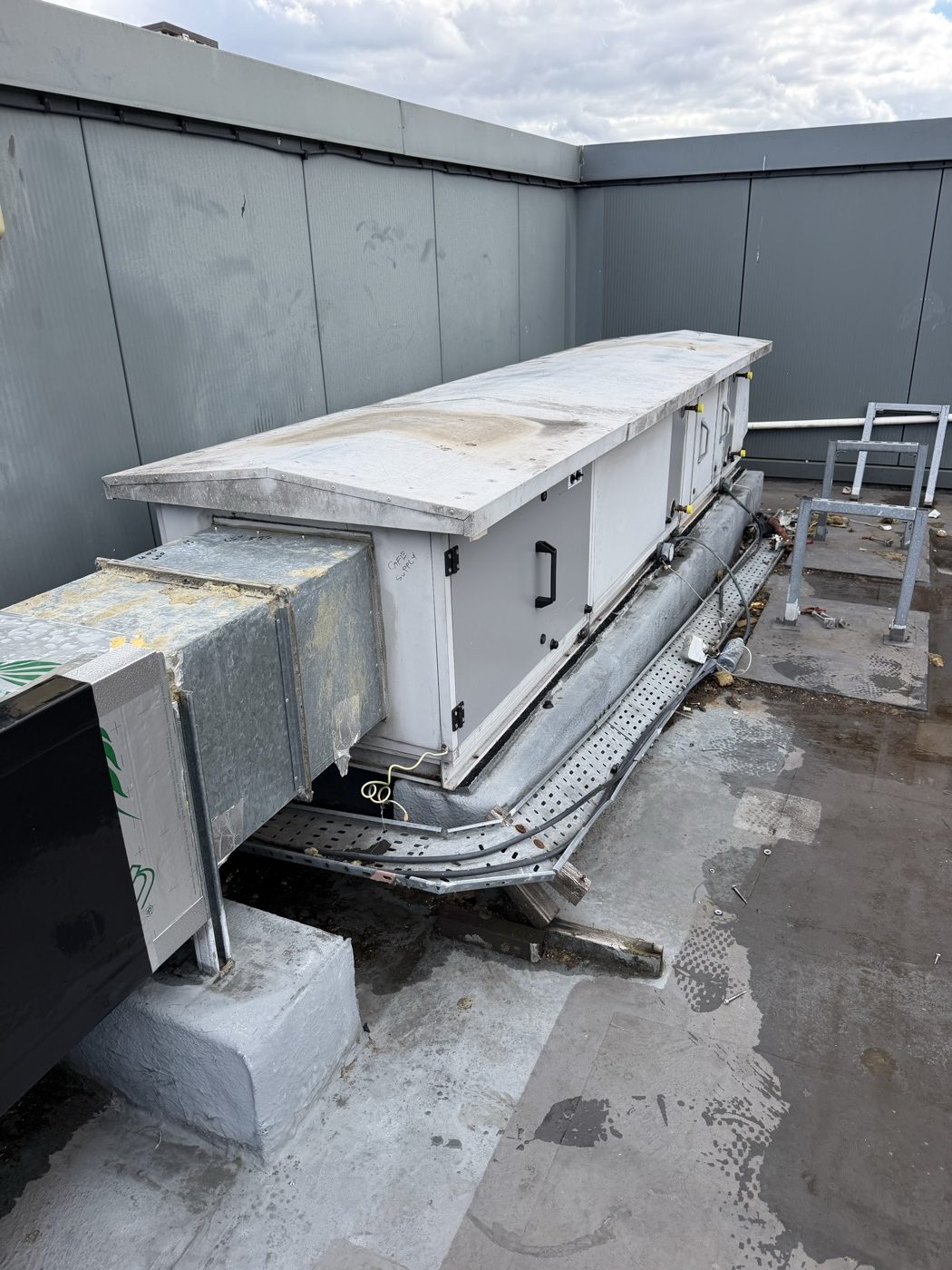 Rooftop air handling unit on plinths with its ductwork and access walkway during a BMS field device replacement
